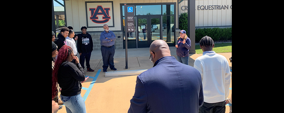 A female presenter speaks to a group of students and teachers welcoming them to a facility