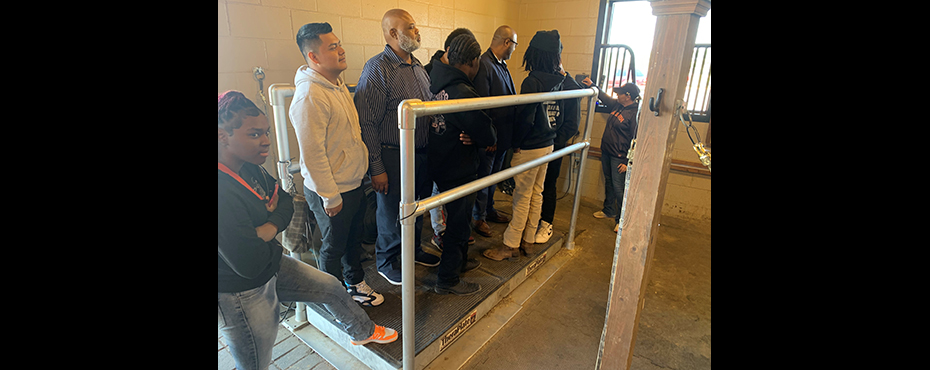 A group of male students and teachers stand on a horse rehab piece of equipment