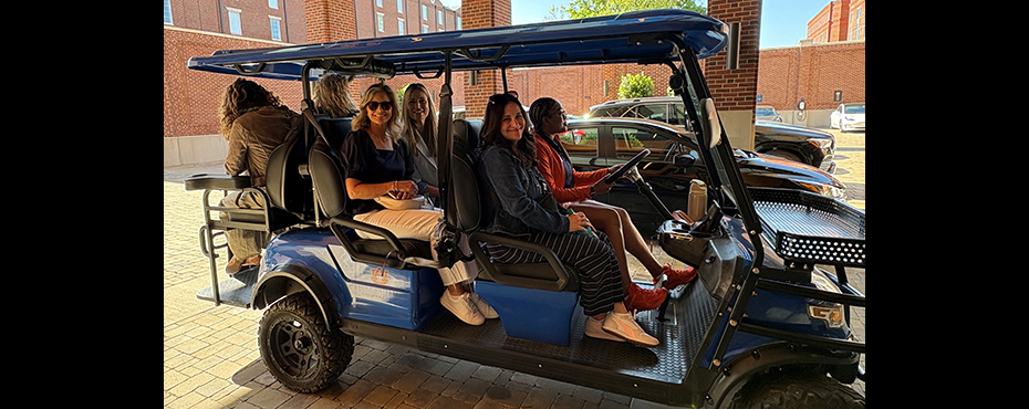 1 female golf cart shuttle driver leads a tour with a group of 5 female guests