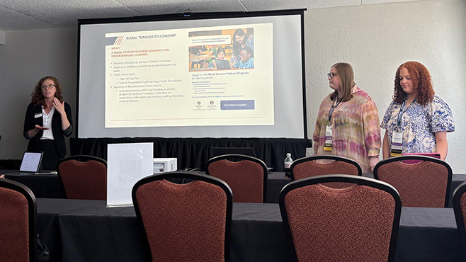Three females in front of a conference room giving a presentation