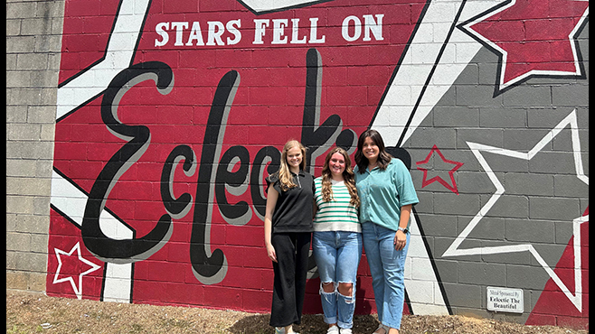Three female fellows standing in front of a mural 'Stars fell on Eclectic'