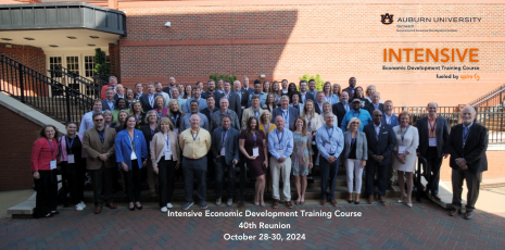 Photo of a group of intensive course alumni standing outside a hotel with text 'Intensive Economic Development Training Course 40th Reunion, October 28-30, 2024'