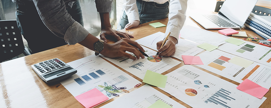 Hands holding pencils and writing on papers scattered on table