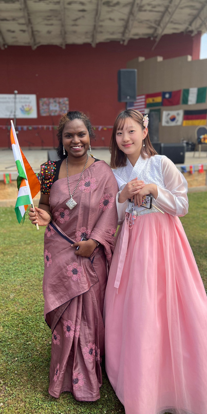 Two females standing in front of the stage wearing cultural attire