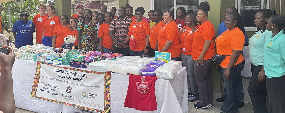 A large group of people standing behind a table holding donations of diapers, baby wipes, and feminine hygiene products.