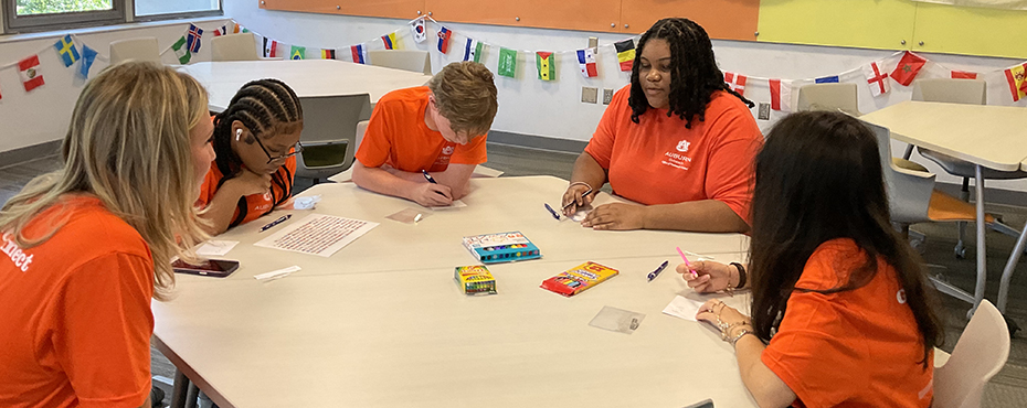 5 people at a table drawing with colored pencils.