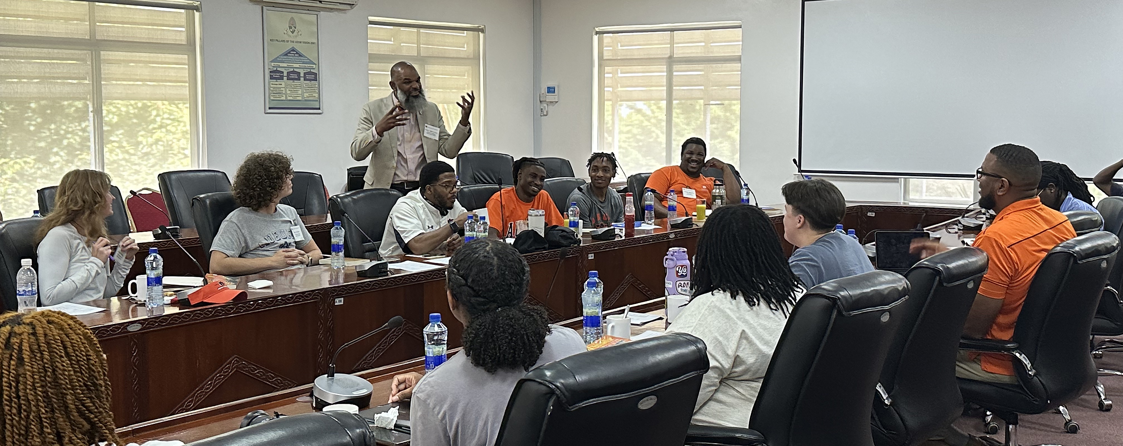 A man standing and teaching while others are sitting at a table.