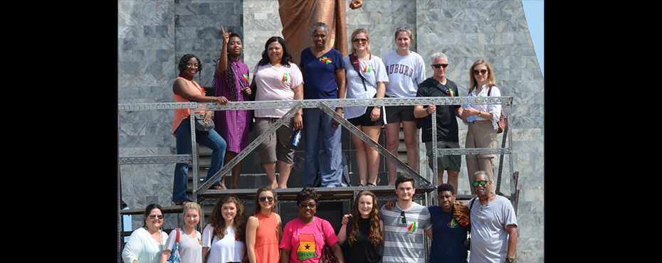 two rows of tourists, one row on a platform behind the other standing in front of a statue