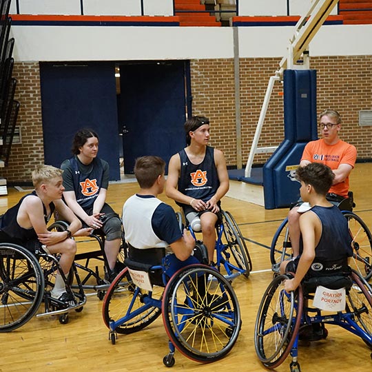 Group of students in wheelchairs in a circle on a basketball court
