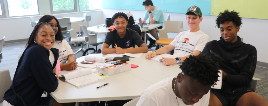 Studnets smile for a photo while sitting at their desks.