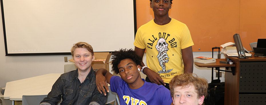 Four male campers smile for a photo in the classroom.