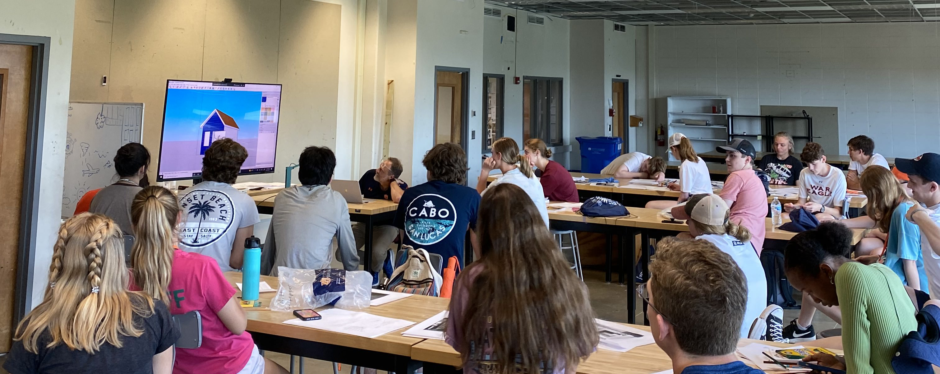 Students sit in the architect studio while they watch an instructional video.