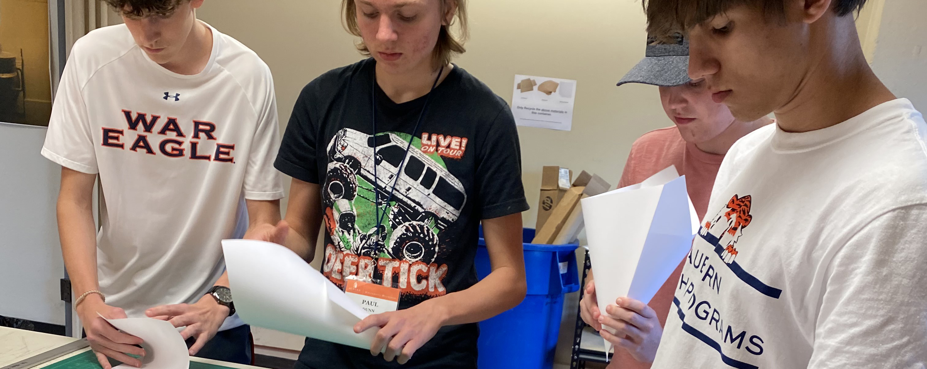Four male students cut paper while working on an architecture project.