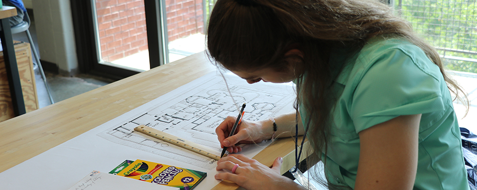A female camper uses a ruler to draw out plans on paper.