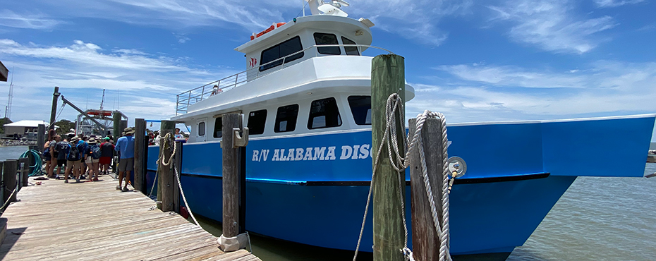 Blue boat sits in water next to dock as students board.