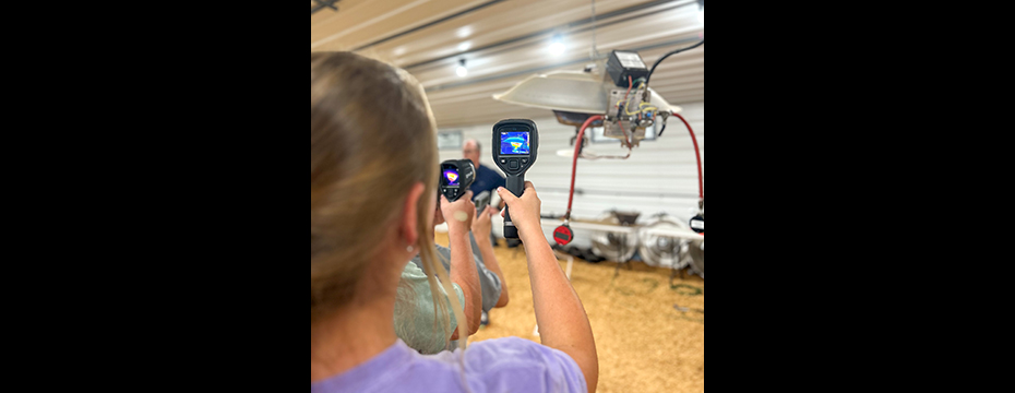 Campers holding heat guns inside a poultry house.