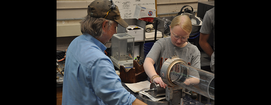 Male instructor overseeing a female camper rolling a pin to make paper.