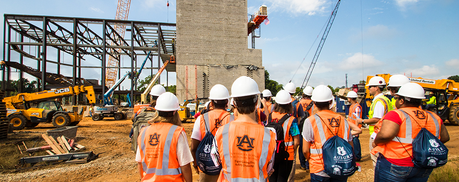 Group of campers in orange vests and hard hats survey construction site.