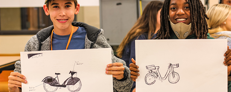Two students hold up drawings of bicycles during industrial design camp