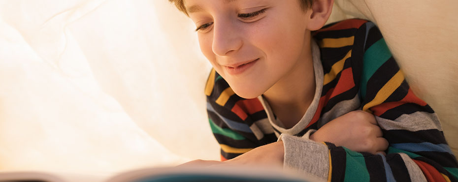 oung male under sheeting reading a book while wearing multi color striped shirt
