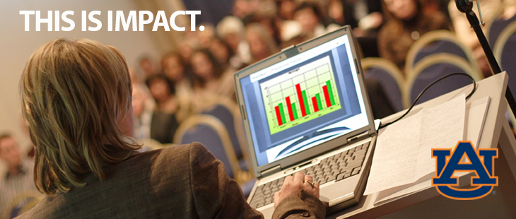 a woman at a podium giving a presentation. the audience is blurred in the background. the picture is taken from over her shoulder and you can see her slides on her laptop. there is a text overlay that says "this is impact"