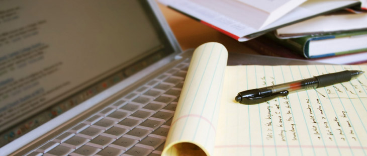 Laptop with notepad with pad on part of the keyboard and a stack of books to the side.