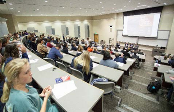 people sitting at rows of tables in a large conference room