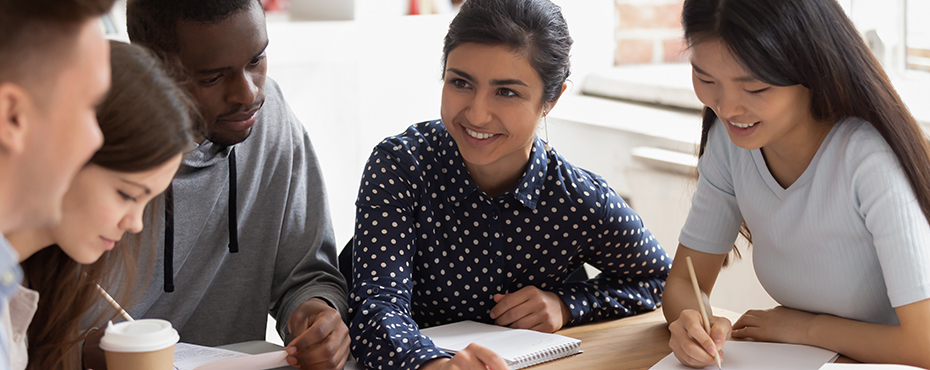 Students of different ethnicities sit around table doing schoolwork