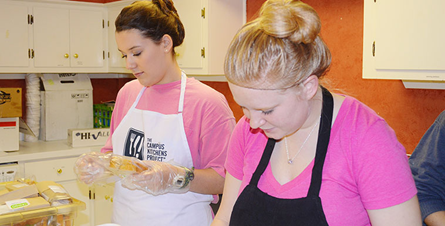 Two students with pink shirts and aprons re-packing cake